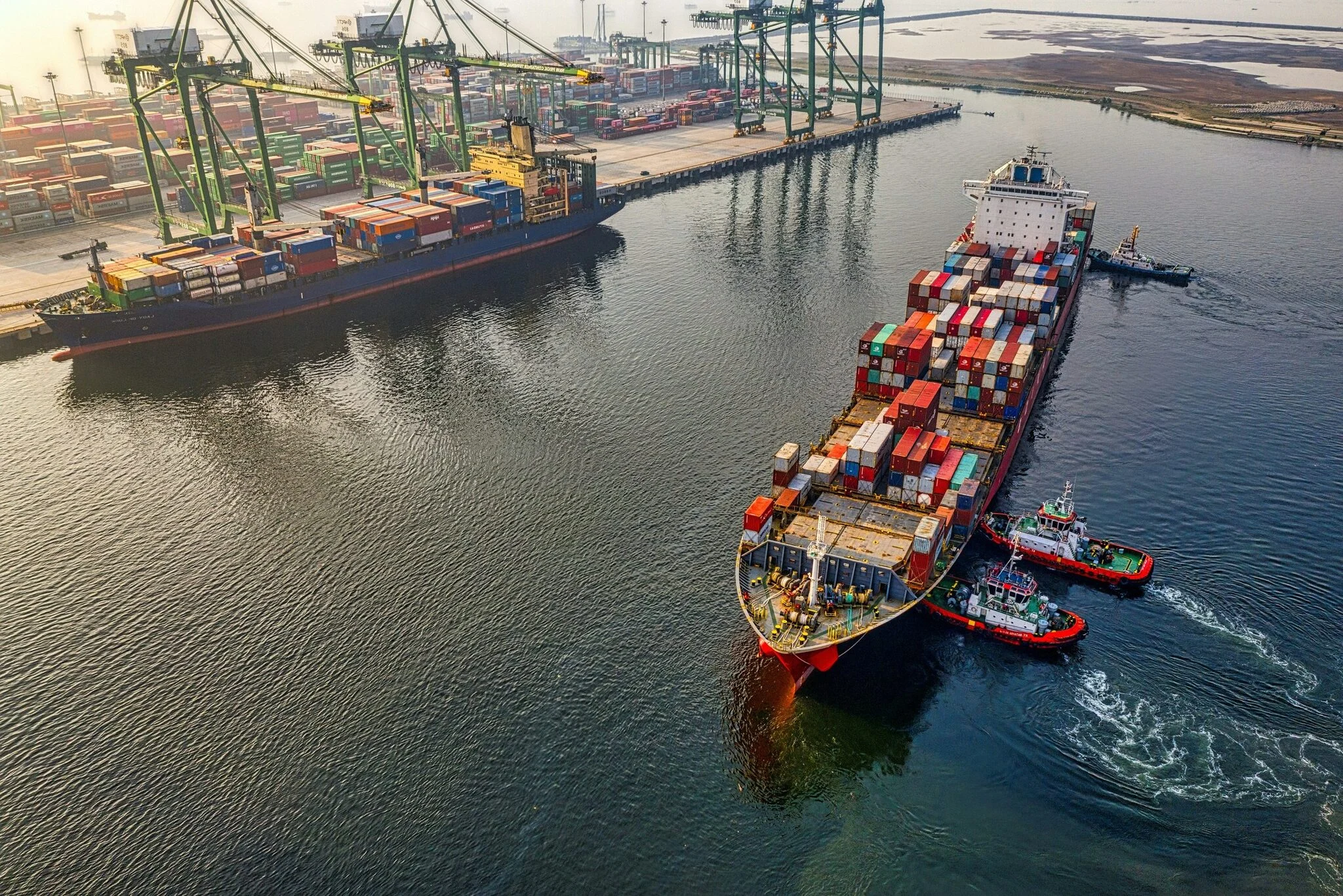 Container ship docking at a port with tugboats